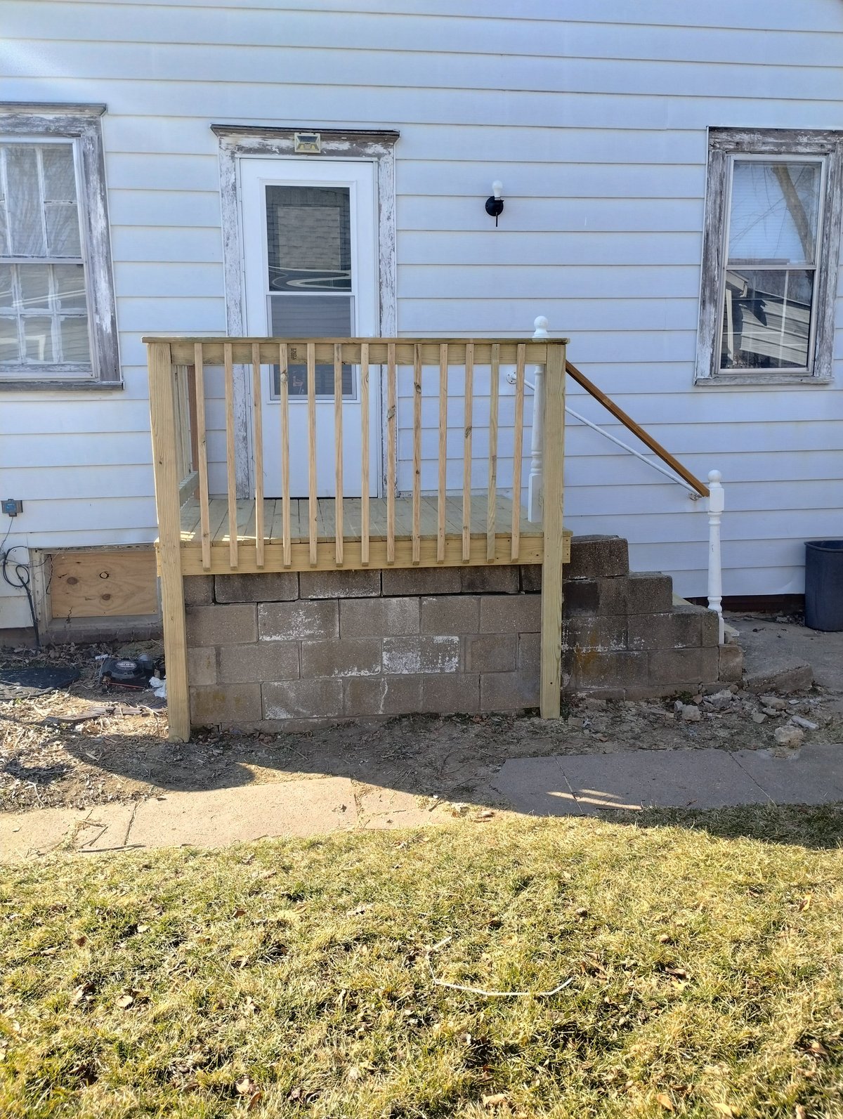Wooden deck railing attached to concrete foundation of light blue house with windows and door