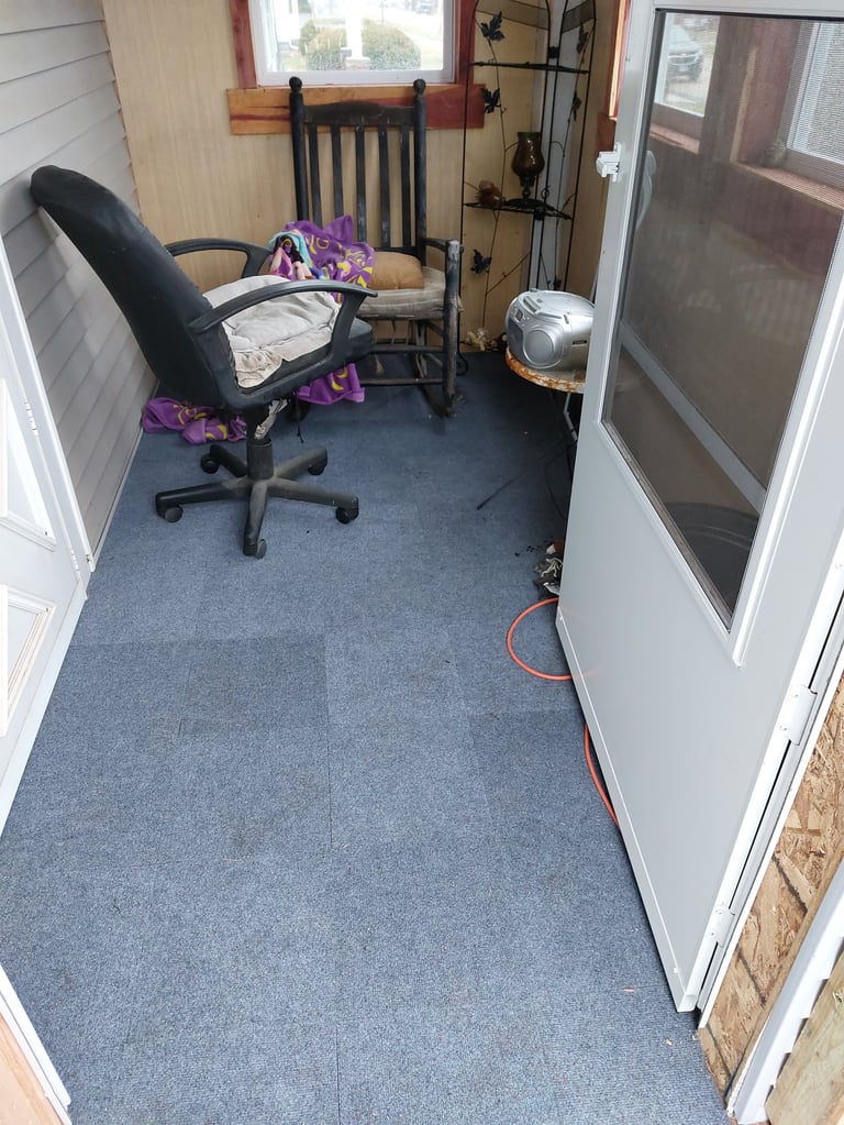 Small room with black office chair, wooden rocking chair, and purple clothing on furniture, with window and doors visible