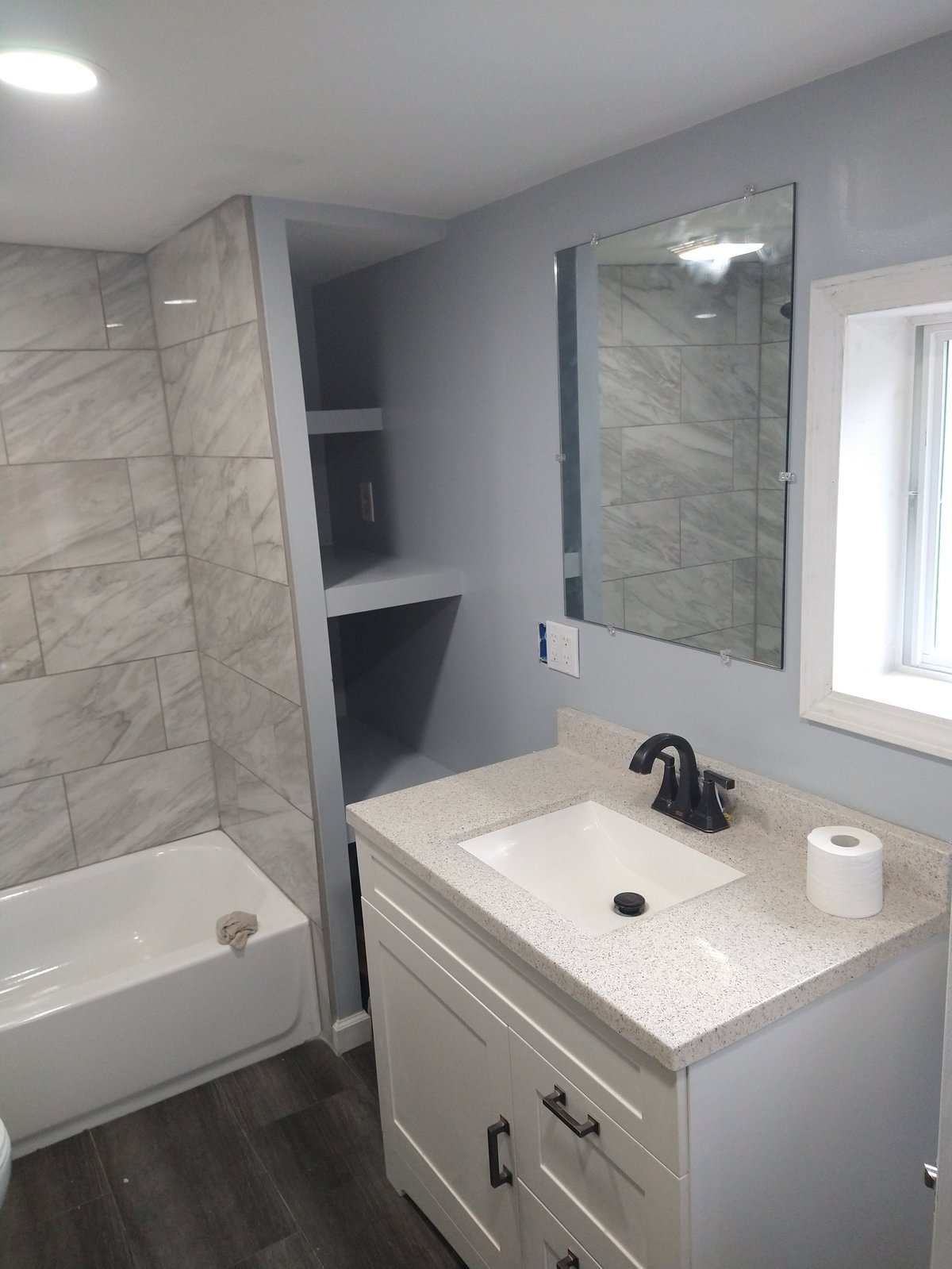 Modern bathroom with white vanity, granite countertop, wall-mounted mirror, glass shower enclosure, and built-in shelving