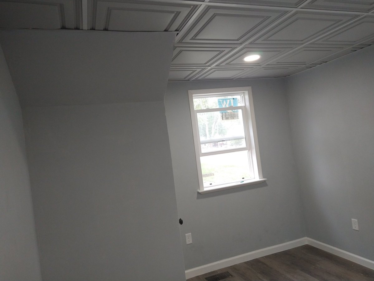 Empty room with white drywall, drop ceiling with recessed lighting, and a window showing brick exterior