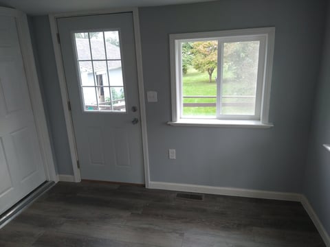 Empty room with gray walls, concrete floor, white door with window panes, and large window overlooking outdoor landscape