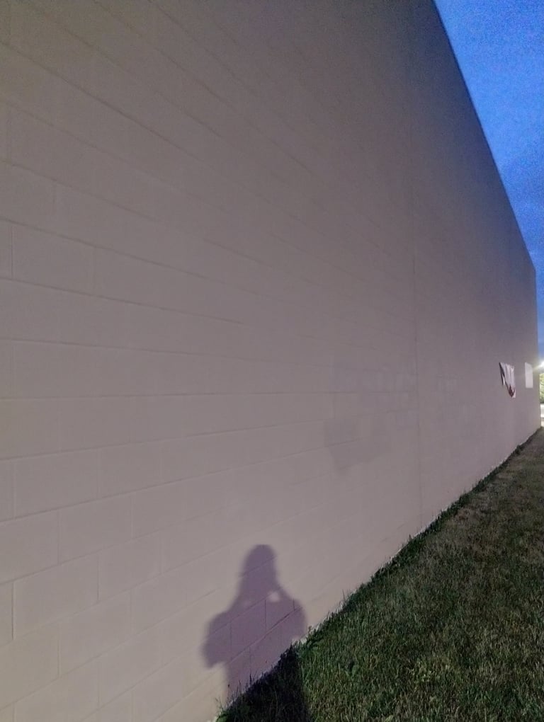 Shadow of a person cast on a white garage wall at dusk with green grass below