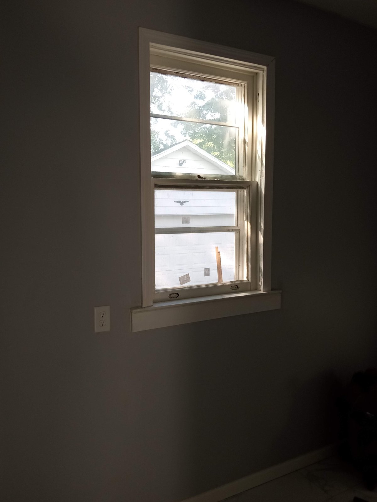 Bright sunlit window with wood frame and four panes mounted on dark wall with outlet visible below