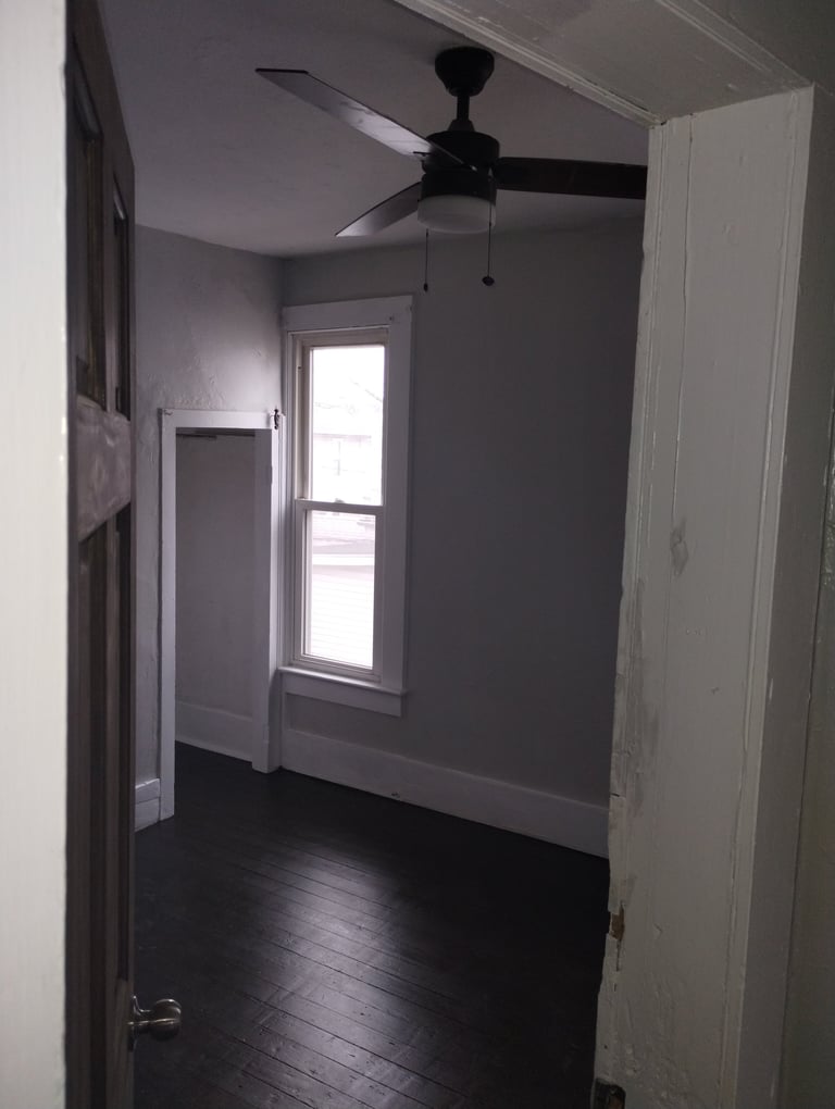 Empty room with dark hardwood floor, gray walls, black ceiling fan, and glass door with window letting in natural light