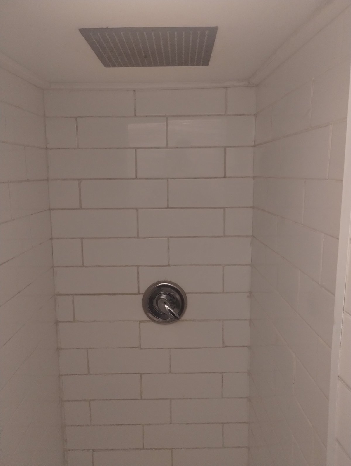 Interior of a shower stall with white subway tile walls, a rain showerhead mounted on the ceiling, and a wall-mounted body spray nozzle