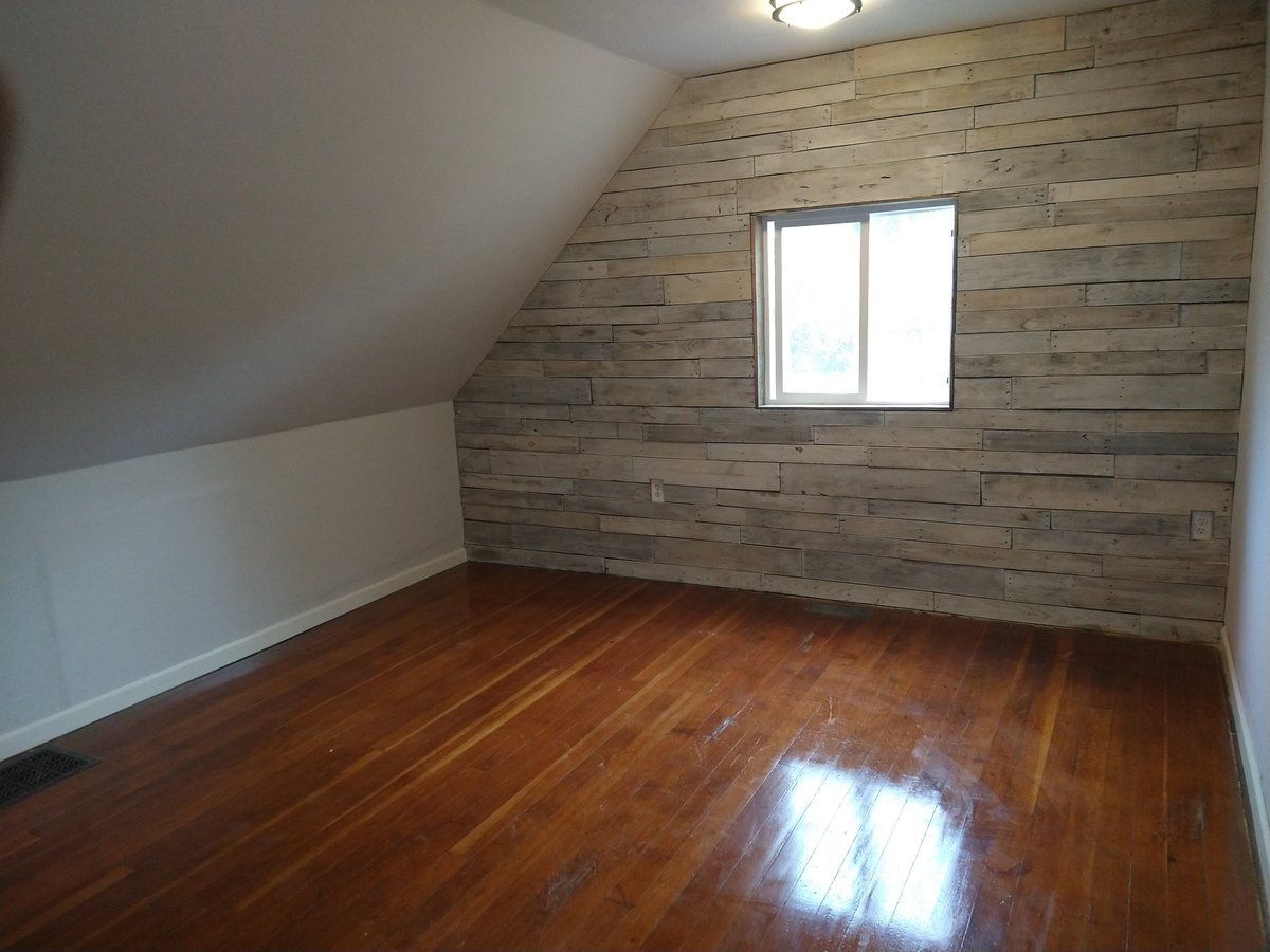 Empty attic room with wooden plank walls, hardwood flooring, and small rectangular window