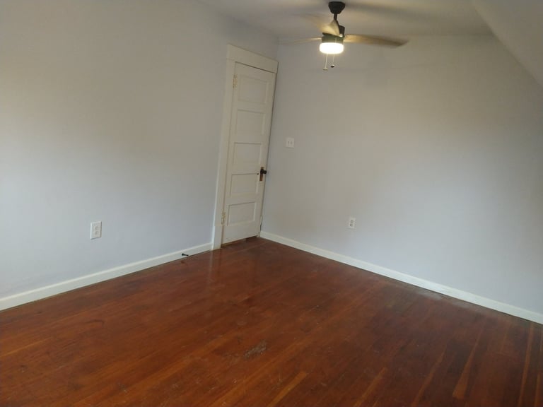 Empty room with hardwood flooring, white walls, ceiling fan, and a narrow white closet door