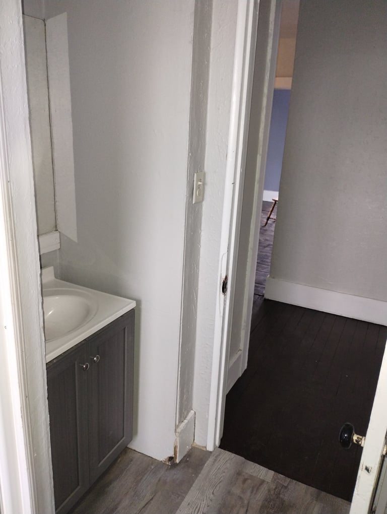 Small bathroom with white walls, dark vanity sink, and open doorway leading to hallway