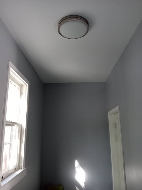 Gray room with window, white door frame, and ceiling-mounted round light fixture