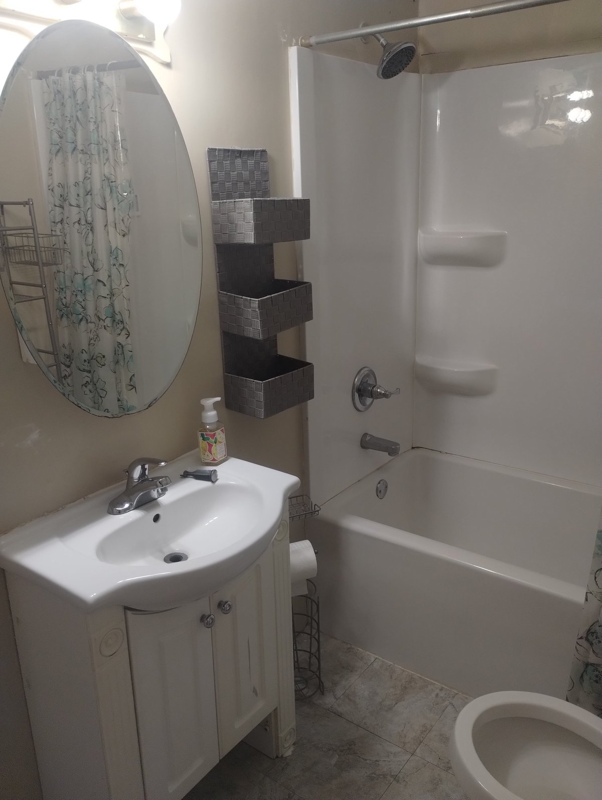 Modern bathroom interior with white sink vanity, round mirror, shower-tub enclosure, black wall shelves, and toilet