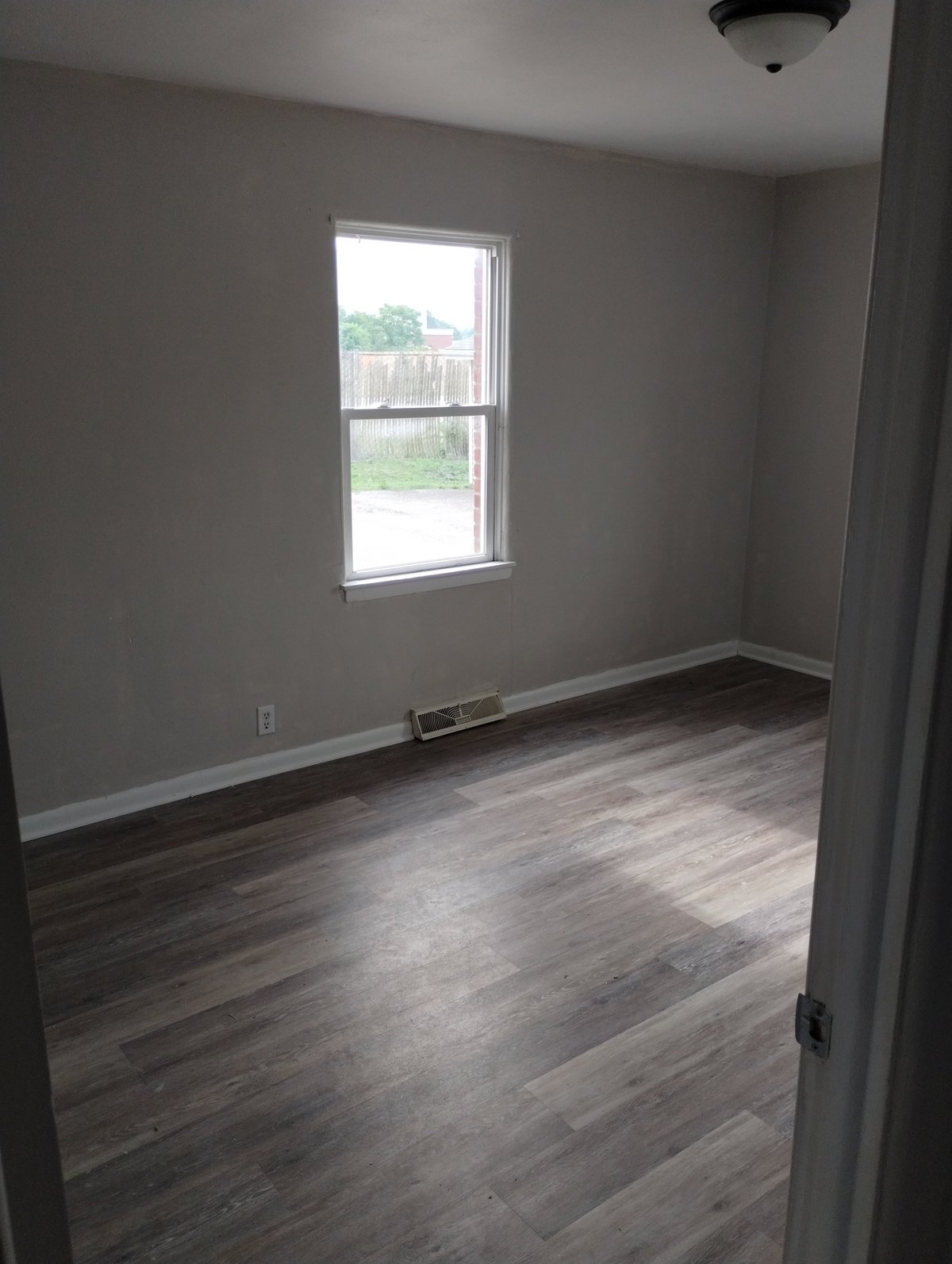 Empty room with gray walls, wood-look flooring, and a large window overlooking a backyard