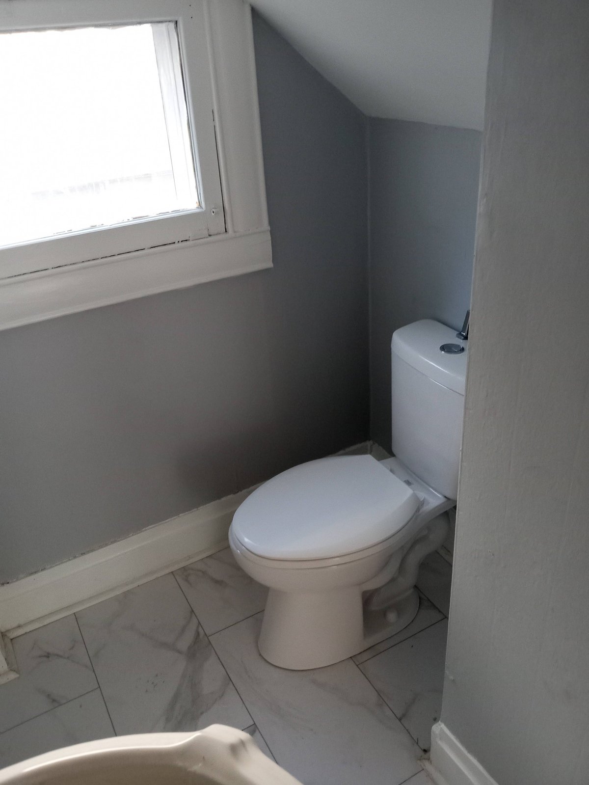 Small bathroom with a white toilet, tiled floor, and window providing natural light from above