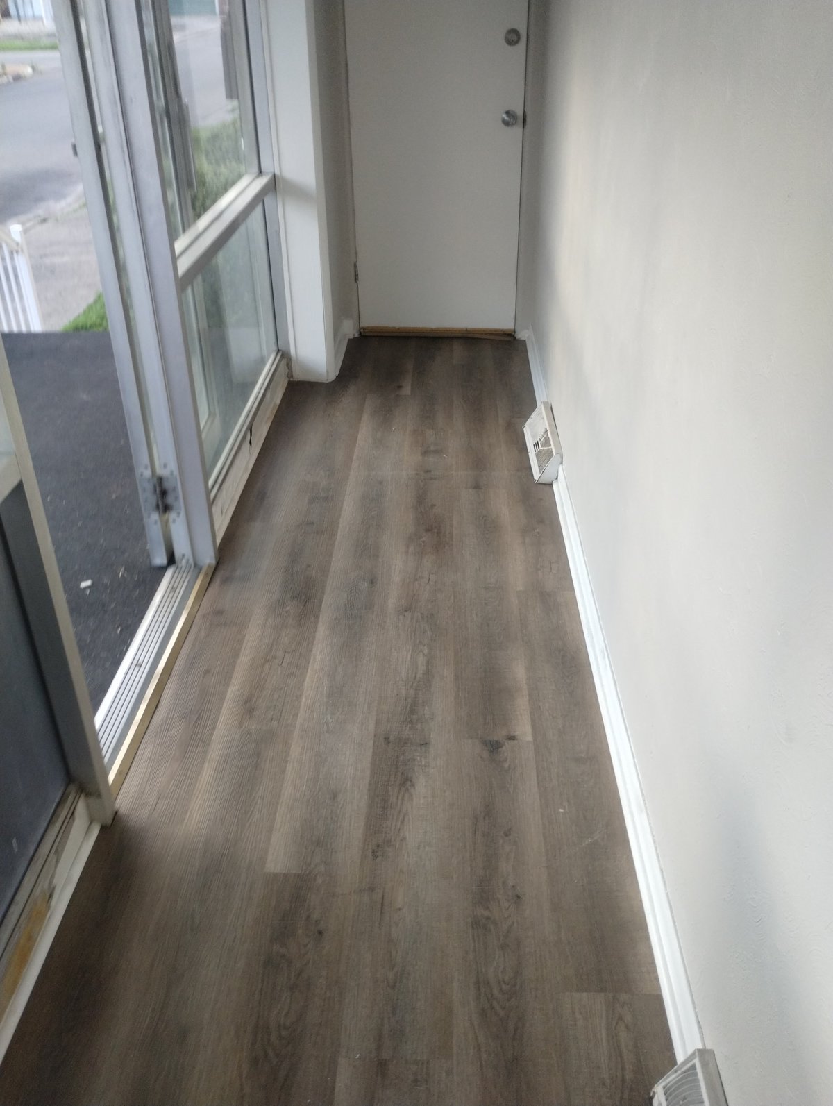 Narrow hallway with dark wood-look flooring, white walls, and glass doors leading to an outdoor area
