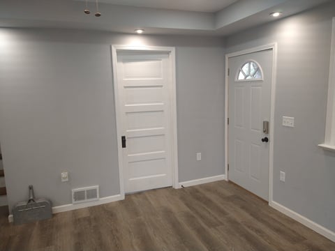 Empty room with light gray walls, white trim doors, recessed ceiling lights, and wood-look laminate flooring