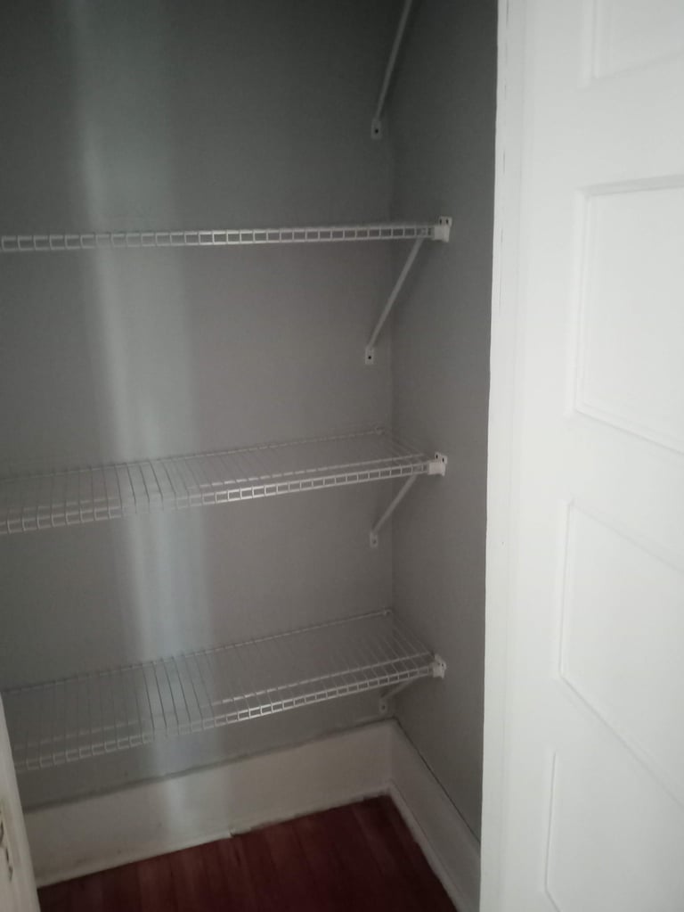 Empty closet with three wire shelves mounted on gray walls and burgundy flooring