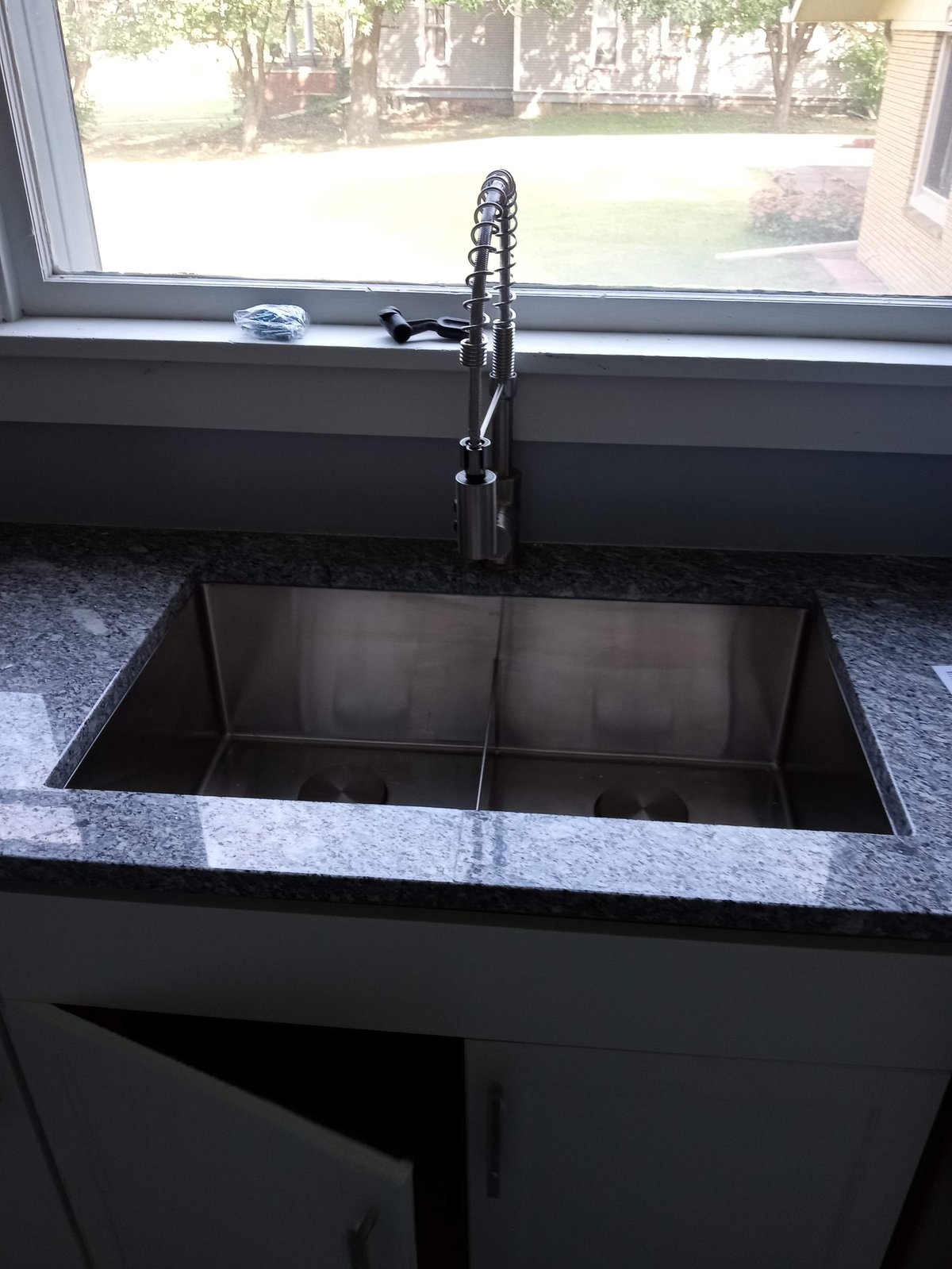 Modern kitchen sink with double compartments, black faucet, and granite countertop by window overlooking backyard