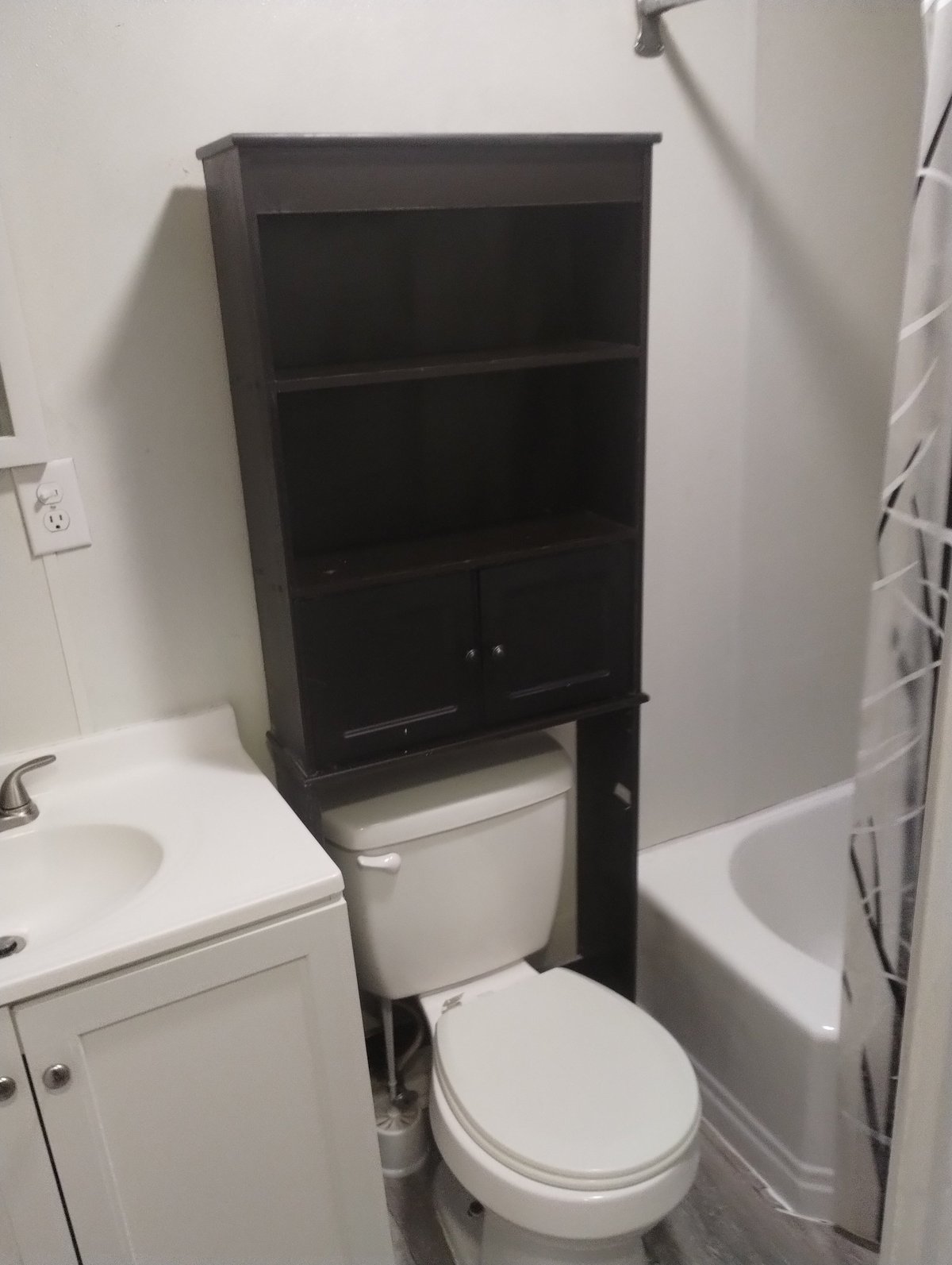 Black over-the-toilet storage cabinet with shelves and lower cupboards positioned above a white toilet in a bathroom