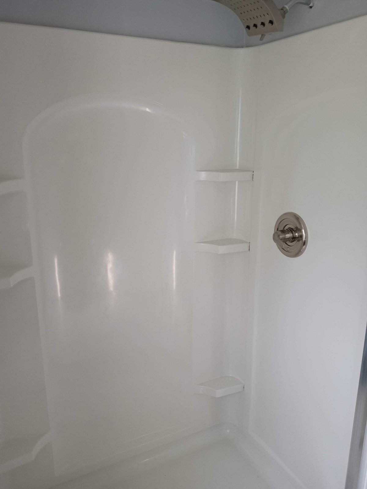White bathroom shower enclosure with three built-in shelves and chrome fixtures on the wall
