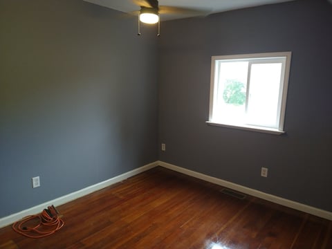 Empty room with dark blue-gray walls, hardwood flooring, ceiling light fixture, window, and orange electrical cord on floor