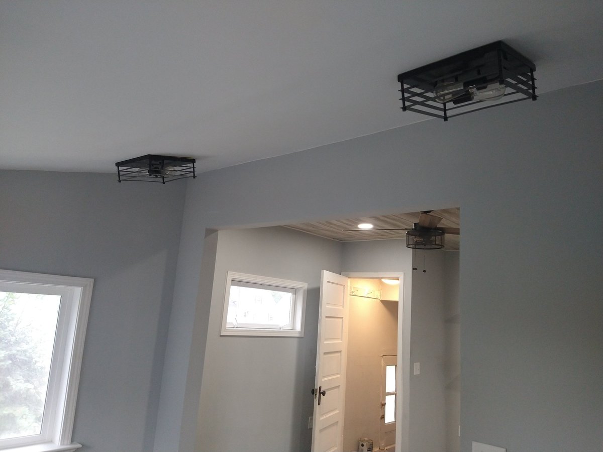 Interior of an unfinished room with drywall, white door, window, and metal ceiling fixtures mounted on the walls and ceiling