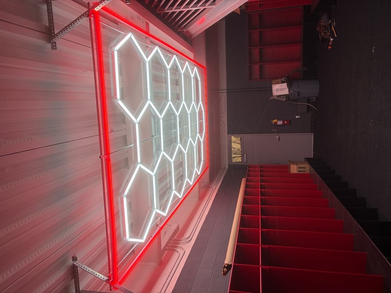Neon sign with red and white hexagonal pattern on dark wall above red stairs in modern interior