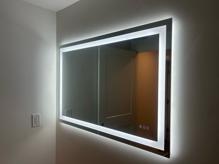 Modern LED-backlit bathroom mirror mounted on a white wall with illuminated white frame and control buttons.
