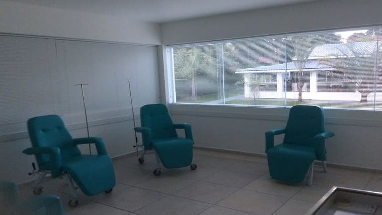 Empty medical or therapy room with three teal recline chairs on wheels arranged in a space with large windows overlooking an outdoor courtyard