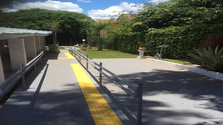 Modern pathway with yellow safety line and metal railings, surrounded by lush green landscape and mountains under blue sky