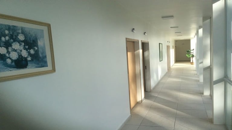 Bright, modern hallway with white walls, recessed lighting, framed artwork, and doors leading to individual rooms