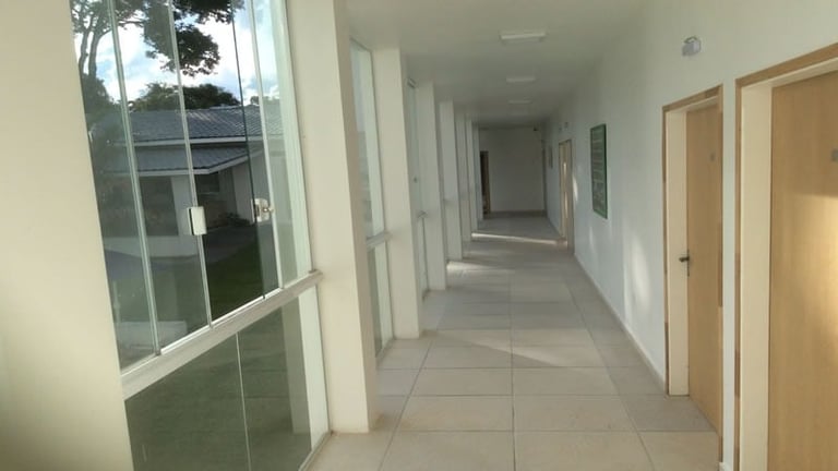 Long empty hallway in a modern office or medical building with white walls, tiled floor, multiple doors, and large windows on the left