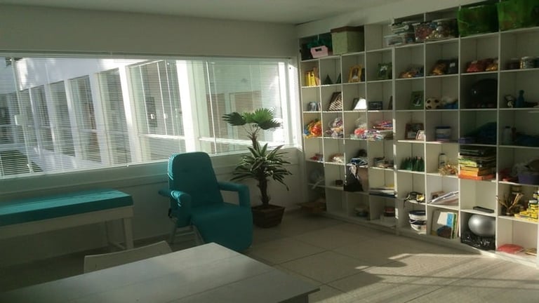 Modern office space with teal desk, chair, shelving unit with collectibles, potted plant, and city skyline visible through windows
