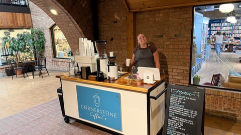 The owner of Cornerstone Coffee Co standing behind the blue cart in the Ice House Mall lobby