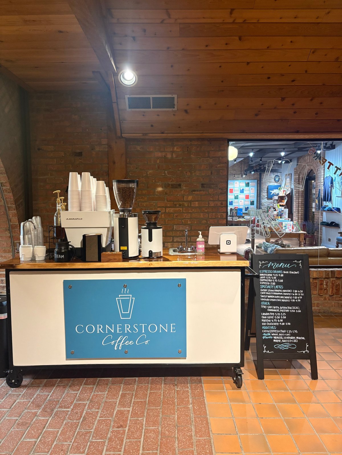 Cornerstone Coffee Co. mobile coffee cart with blue signage in an indoor brick venue, equipped with espresso machine and supplies.