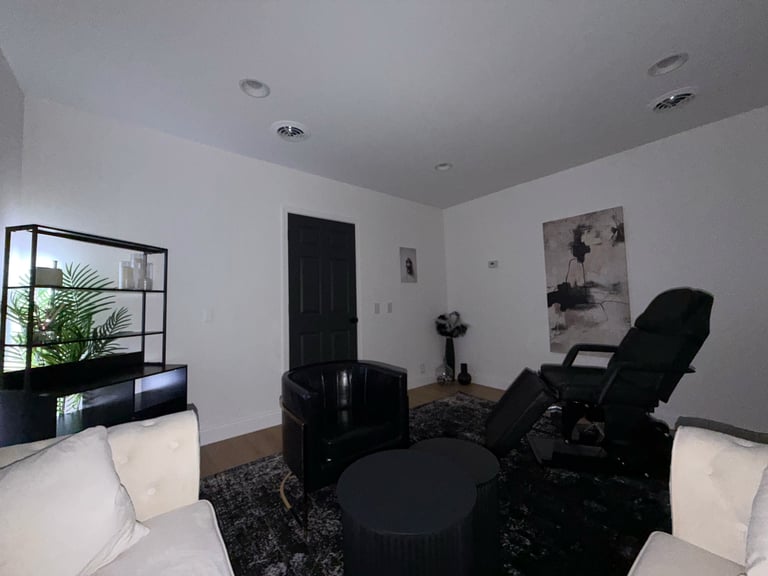 Modern living room with white walls, black recline chair, white couches, black round table, and framed artwork on walls