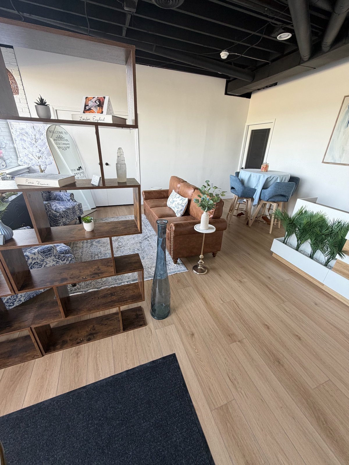 Modern office waiting room with wooden furniture, blue accent chairs, potted plants, and floating shelves against white walls