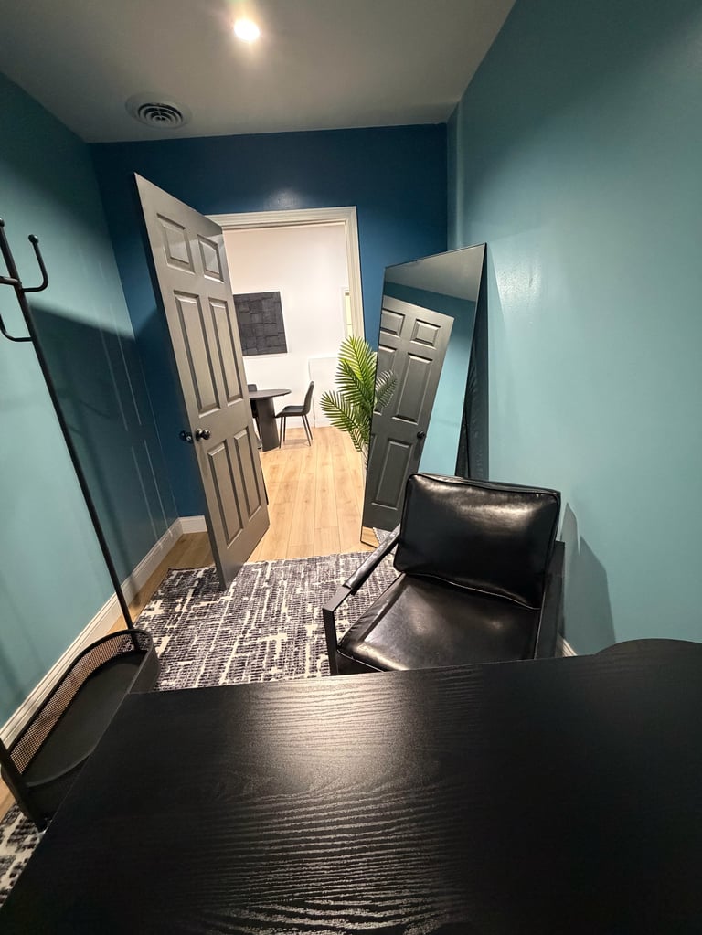 Modern office hallway with turquoise walls, black leather chair, dark desk, and doorway leading to bright interior space