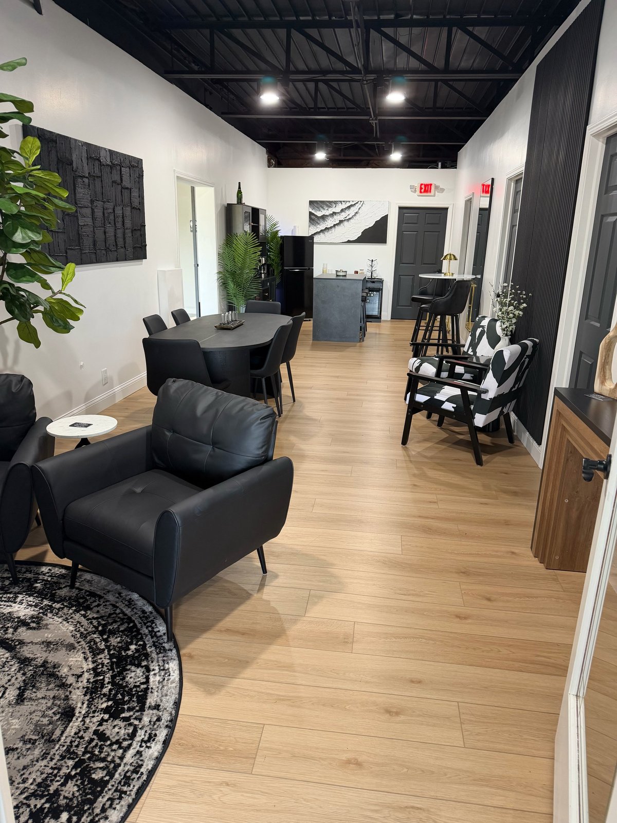 Modern office or salon interior with black furniture, wood flooring, white walls, and industrial ceiling with track lighting