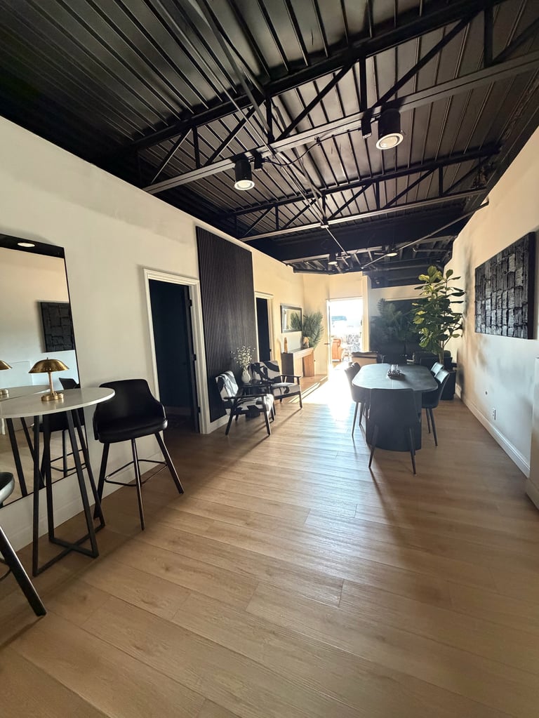Modern office or showroom with exposed metal ceiling, wooden flooring, white walls, and black furniture including desks and chairs