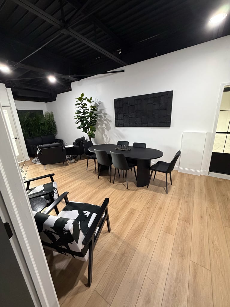 Modern office space with black furniture, wooden flooring, white walls, black ceiling, and a potted plant