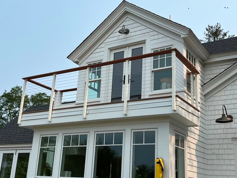 Modern two-story white house with second-floor deck and brown railings against clear blue sky