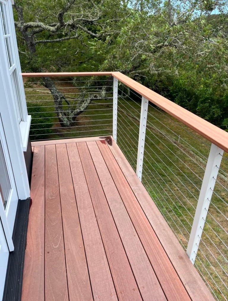 Modern wooden deck with metal cable railing overlooking green trees and forest landscape