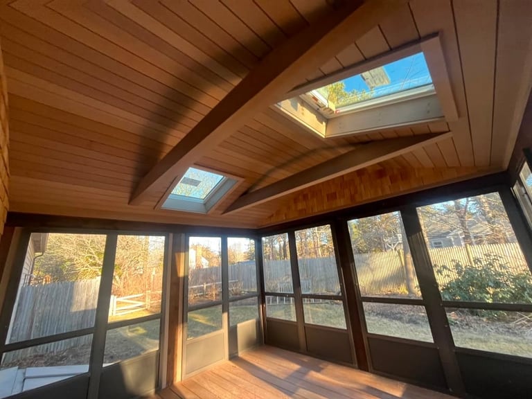 Interior of a bright wooden sunroom with skylights and glass doors overlooking autumn forest