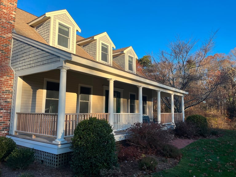 Colonial-style brick home with yellow trim, white porch columns, and dormers on a clear sunny day