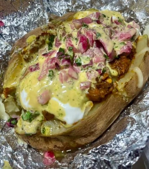 Loaded birria baked potato topped with shredded birria, cheese, sauce and fresh onion