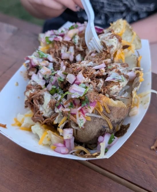 Loaded baked potato topped with birria, cheese, sauce and fresh onions