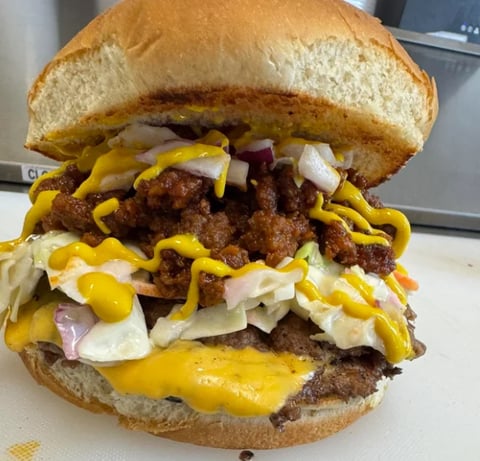 Loaded cheeseburger on toasted bun with crispy bacon, melted cheese, onions, and mustard