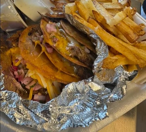 Grilled fish wrapped in foil with golden fries and red onions served on parchment paper