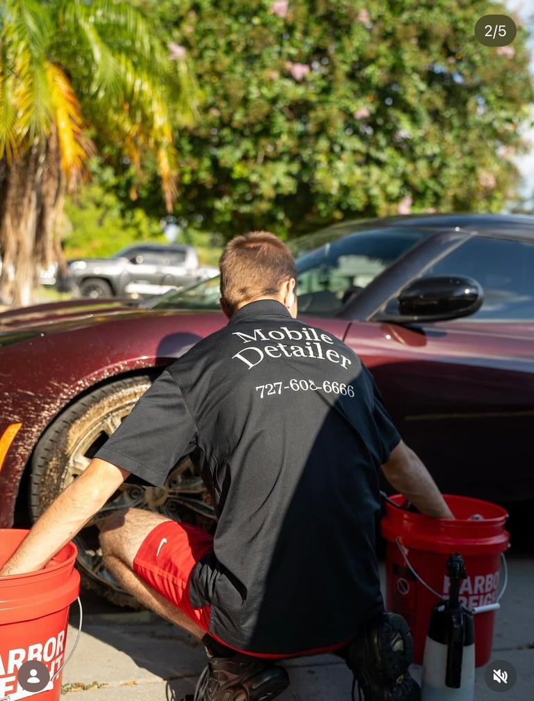 Mobile detailer wearing black shirt polishing a red car exterior with bucket nearby