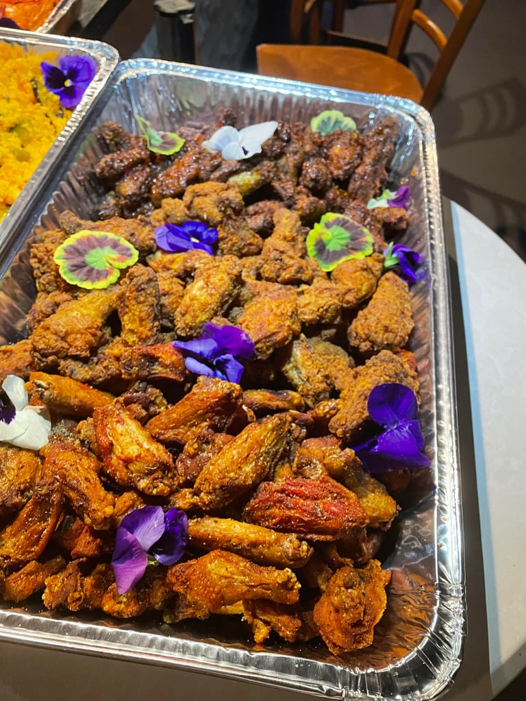 Aluminum tray of fried chicken and shrimp garnished with purple flowers and edible greens, served at a catered event