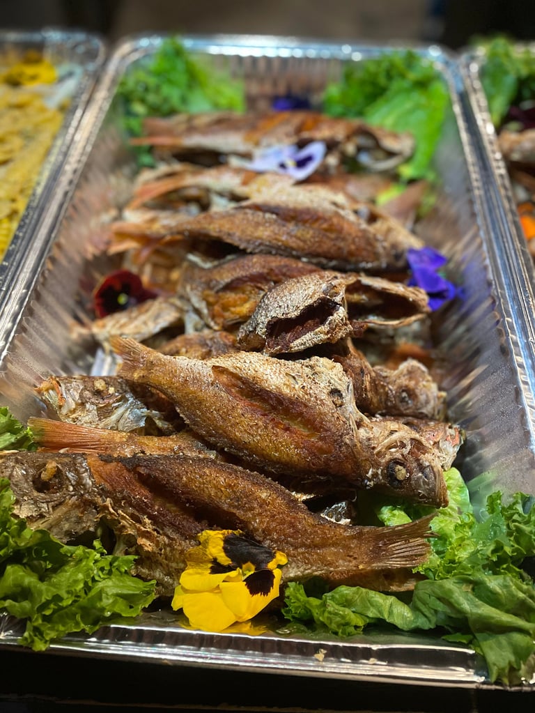 Grilled whole fish arranged on a clear tray with fresh lettuce and yellow flower garnish
